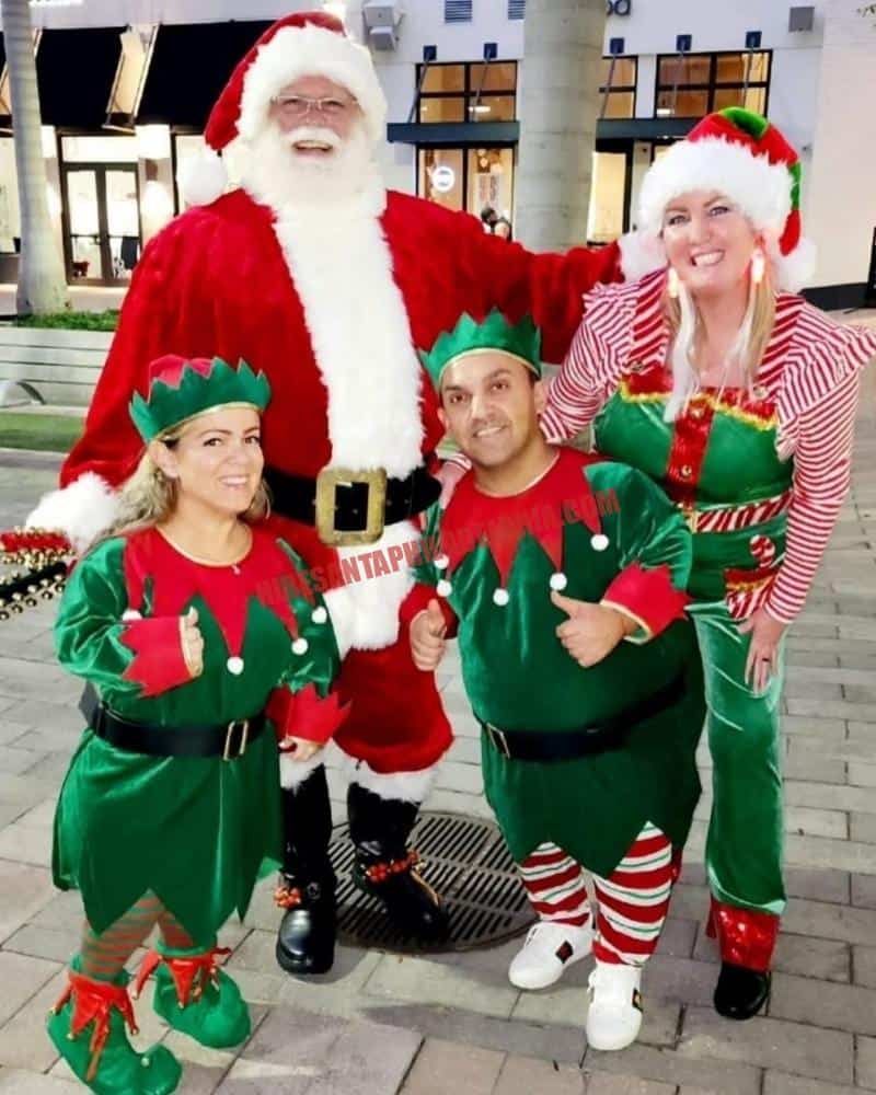 Santa for hire in West Chester, PA outdoors with three elves at dusk.